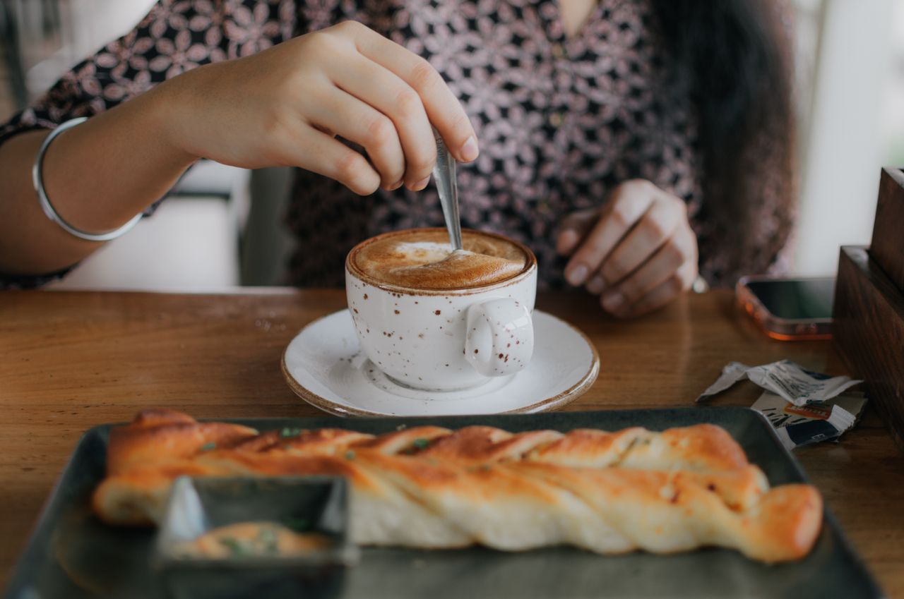 About A woman enjoying coffee and pastry at a café, stirring her drink while seated indoors.