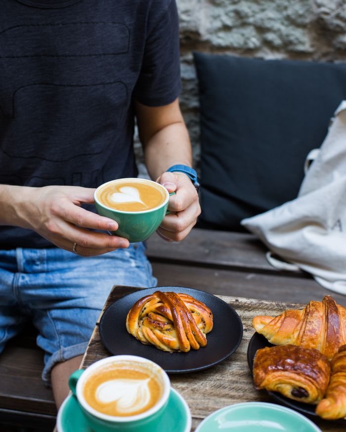 Home A person enjoying coffee with a heart latte art and pastries on a cozy outdoor bench.
